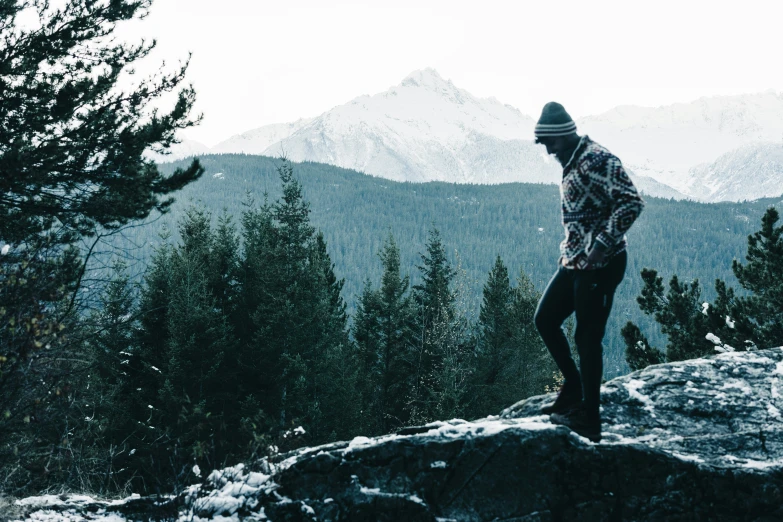 a man standing on top of a snow covered cliff next to a mountain