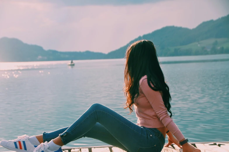 a young woman sitting on a dock with the lake in the background