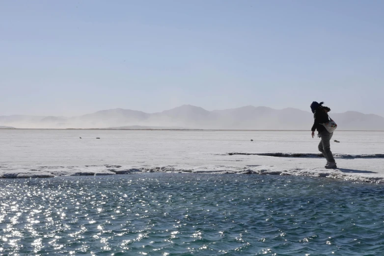 a person walking in the middle of an ocean near some mountains