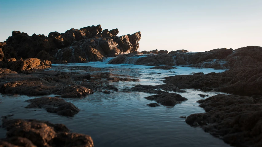 the surface of the water near the rocks are covered in sand