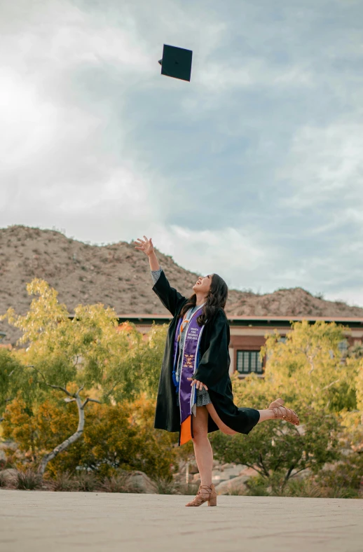 a woman wearing glasses, graduation gown and a hat tossing a tassel in the air