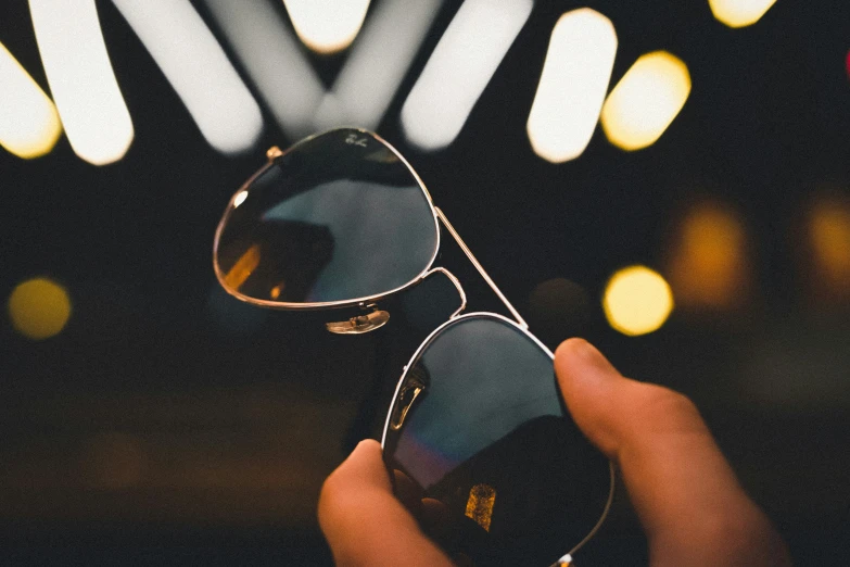 person holding onto sunglasses with blurry background