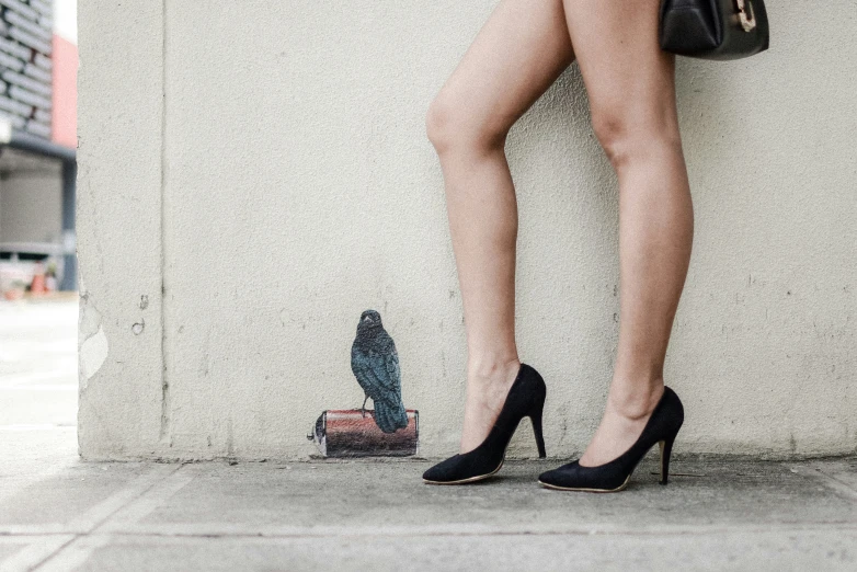 a woman's feet and heels standing near a wall
