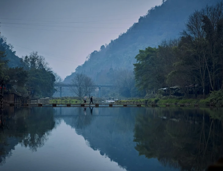 two people standing on a dock in front of a lake