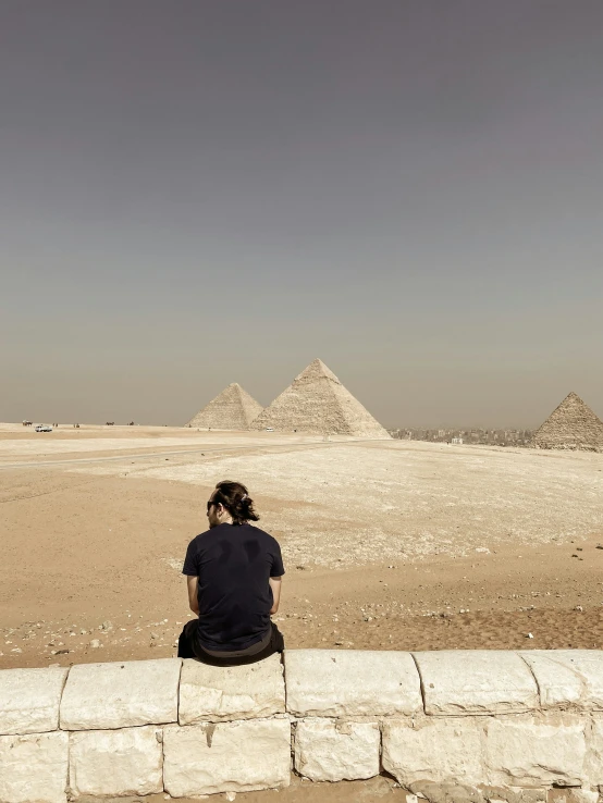 a woman sits on a ledge looking at the pyramids