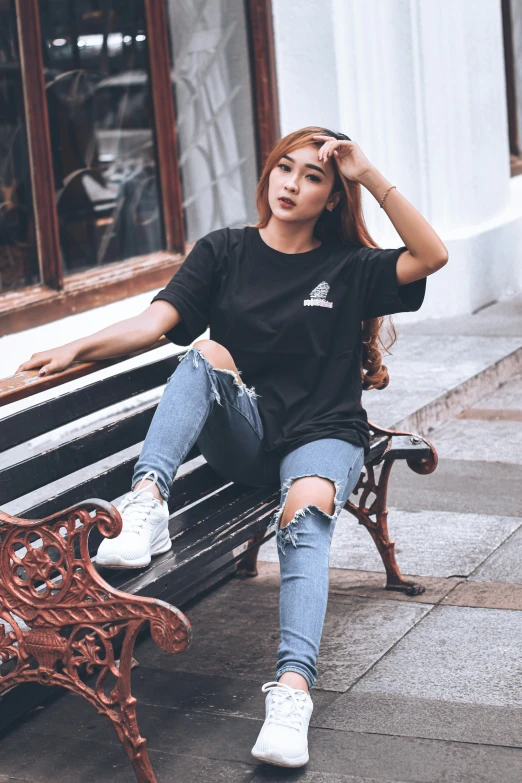 a girl wearing jeans and sneakers sitting on a bench