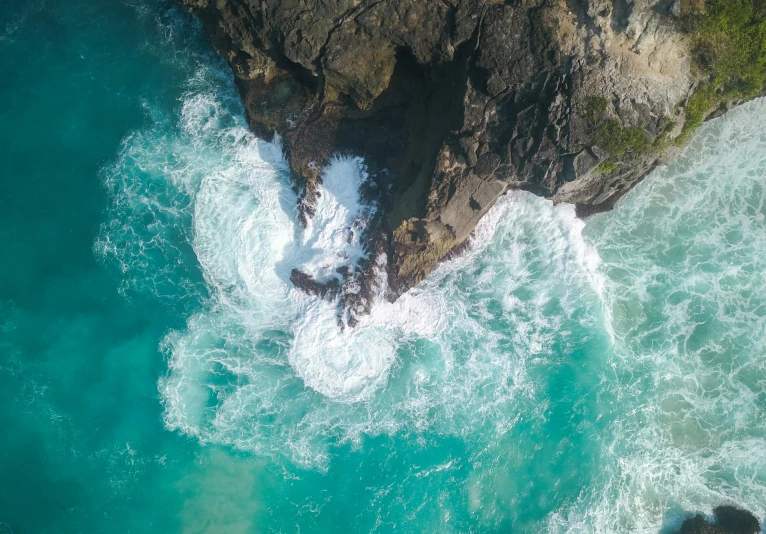 an aerial view shows waves crashing into a cliff, some rocks and cliffs beyond