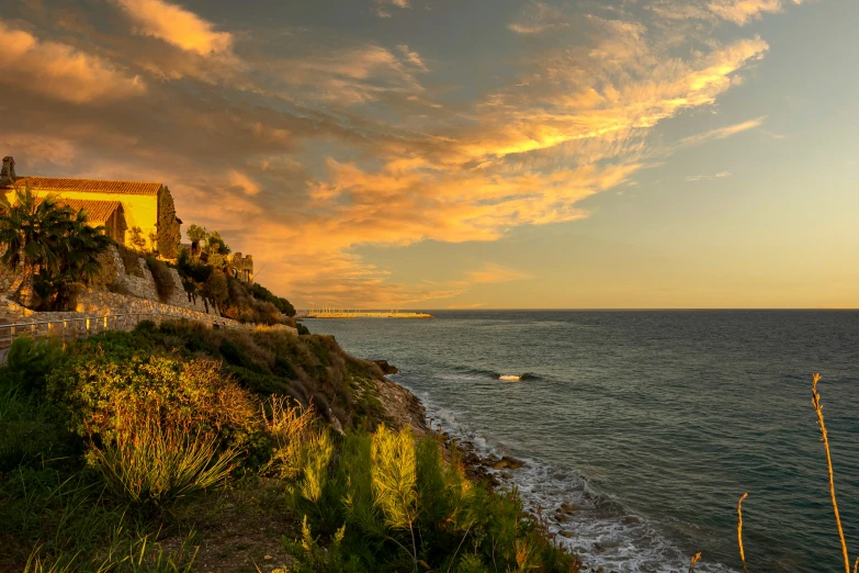 the sun is rising above the ocean and a large building is on a cliff