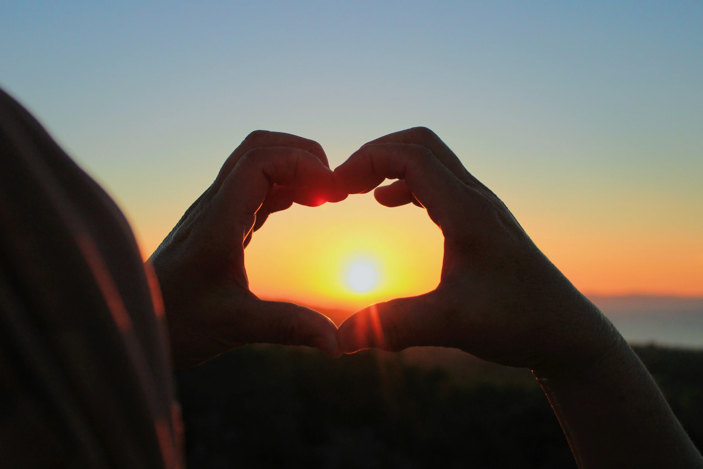 someone making a heart with their hands at sunset