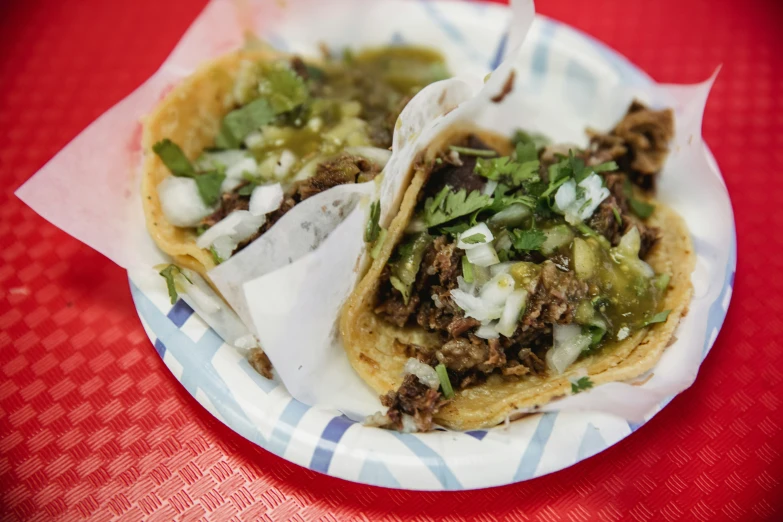 two tacos on a paper plate sitting on a red table