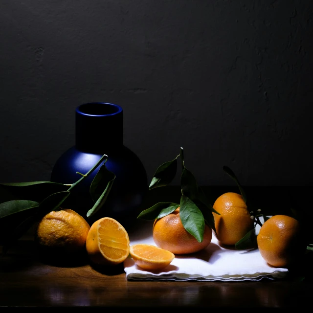 a table holding oranges next to a vase and a napkin