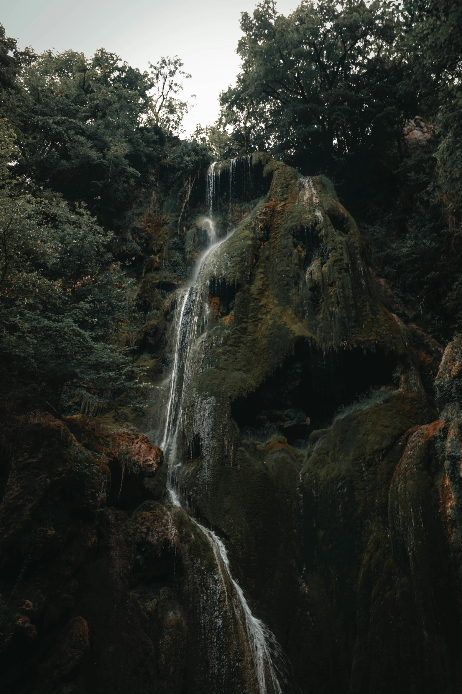 a waterfall in the forest with dark water