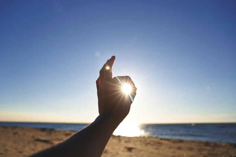a person pointing to the sun on a beach