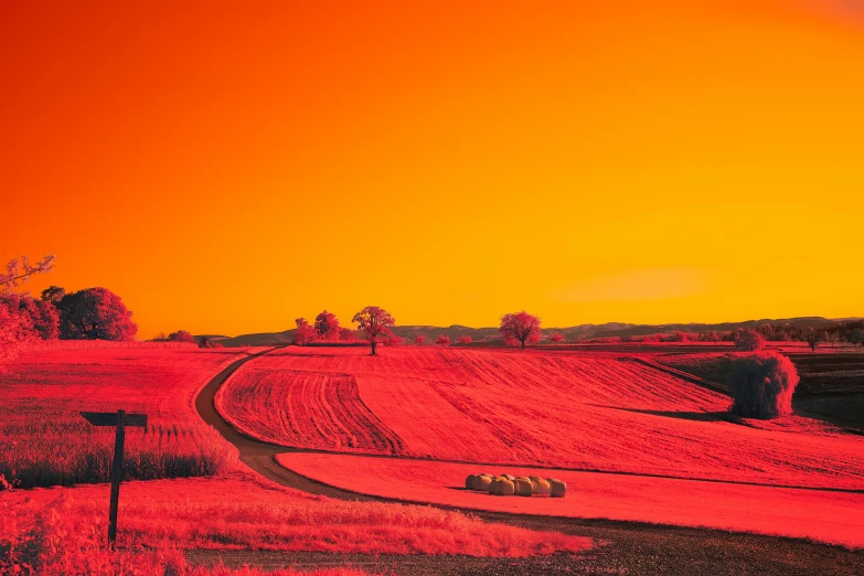 a red sunset with hay bales on the side of a rural road