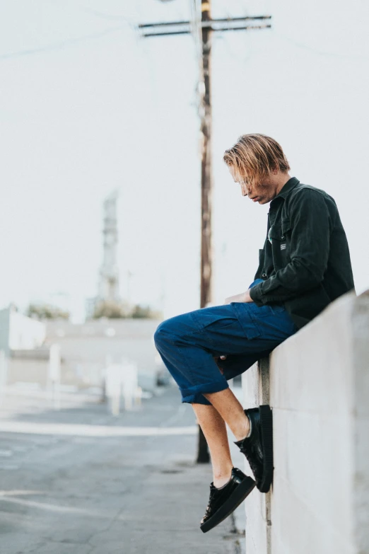 a man in black shirt sitting on wall next to telephone pole