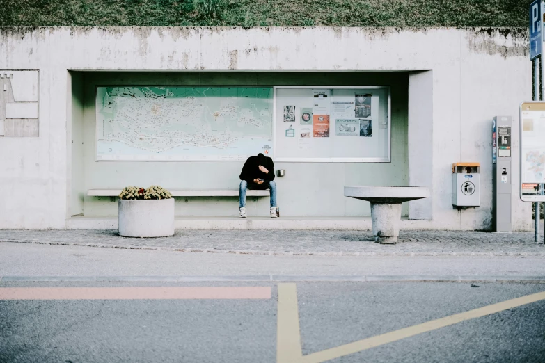 an old man sitting alone in front of a bus stop