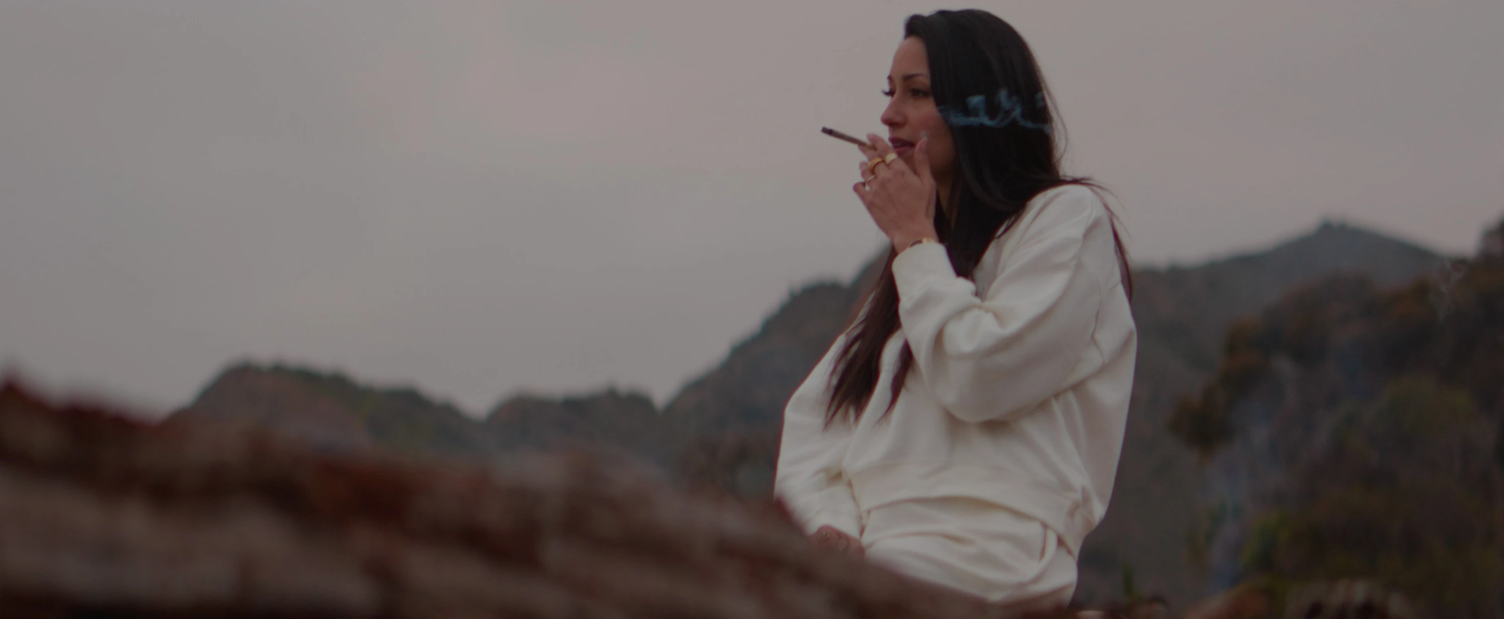 woman in white jacket smoking on a hill