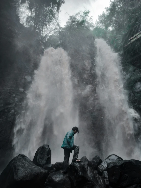 a man standing next to a waterfall on top of rocks