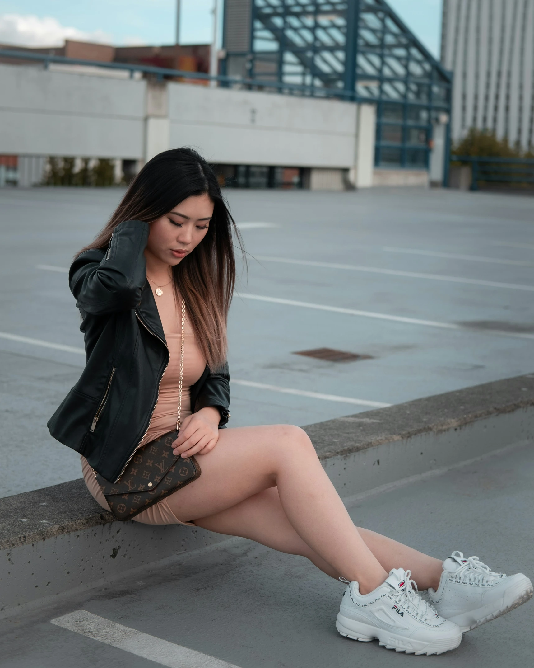 a woman in an open shirt and sneakers sitting next to a parking lot