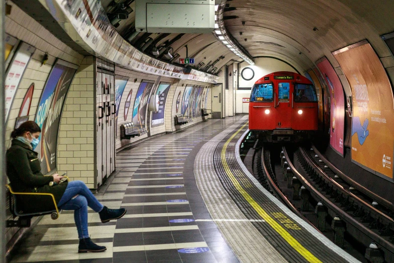 a person sitting at the end of a train platform with a red and red train