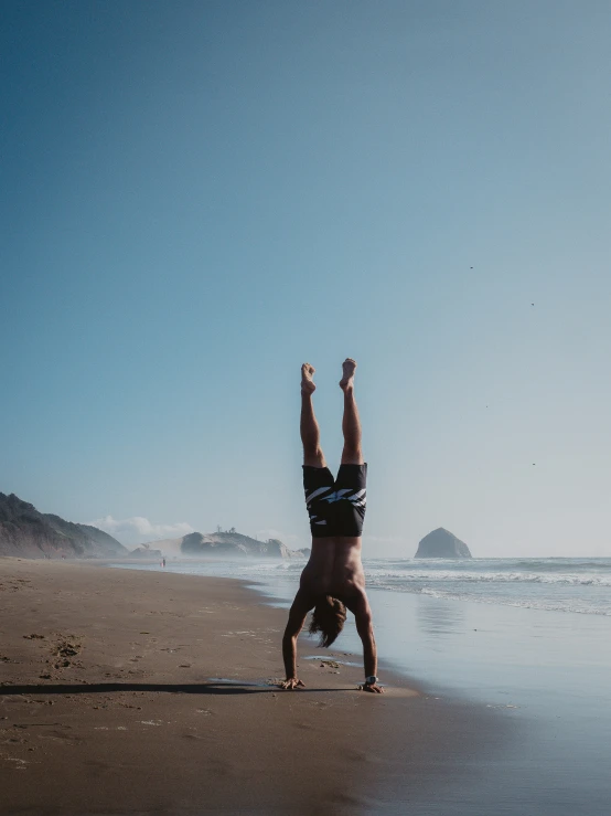 two people doing handstand at the beach with their feet in the air