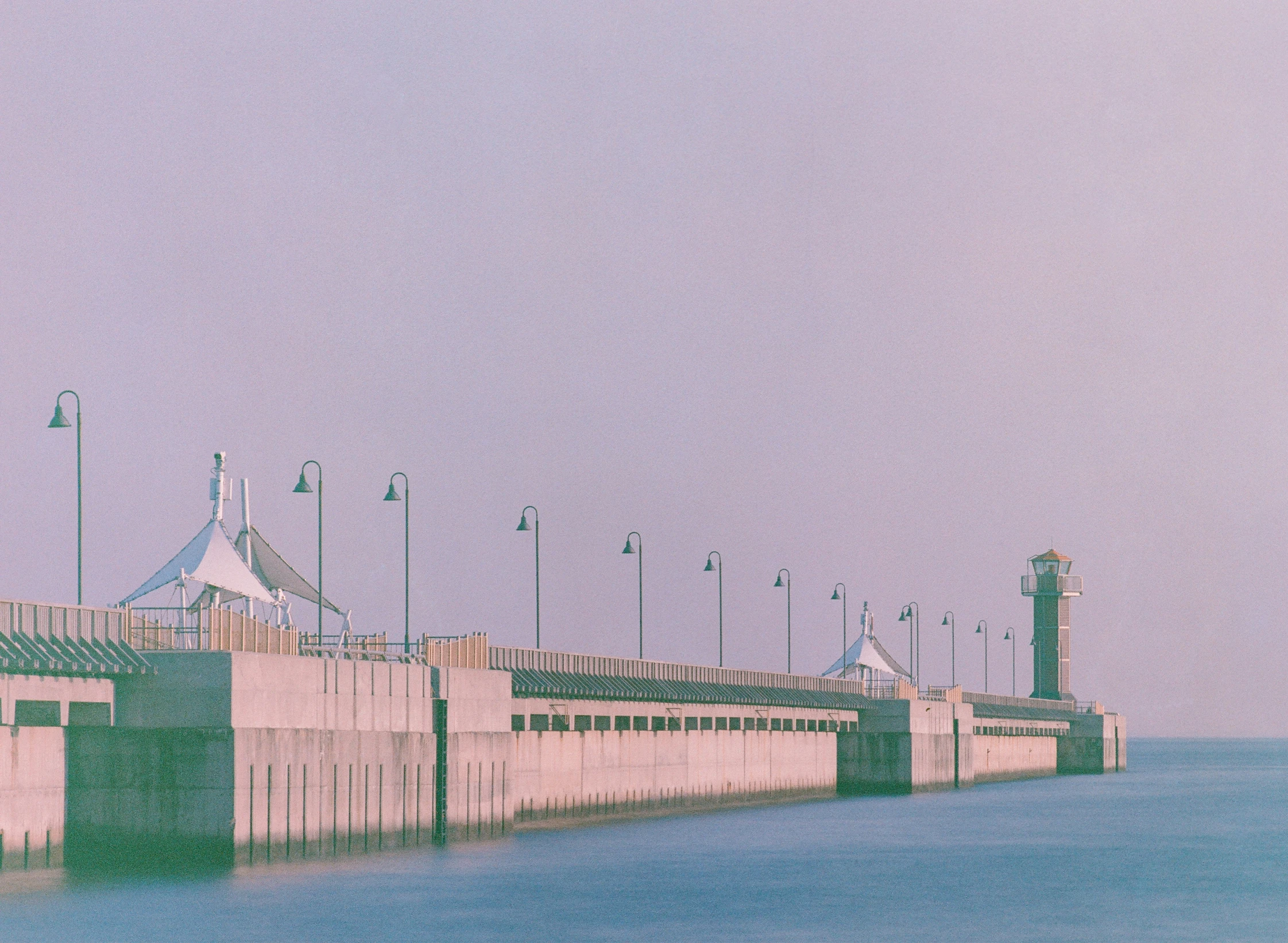 a long wall and some lights on poles next to water