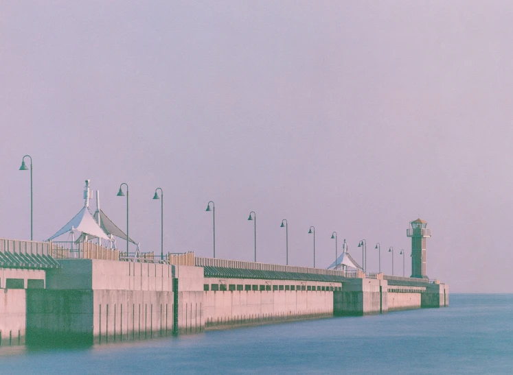 a long wall and some lights on poles next to water