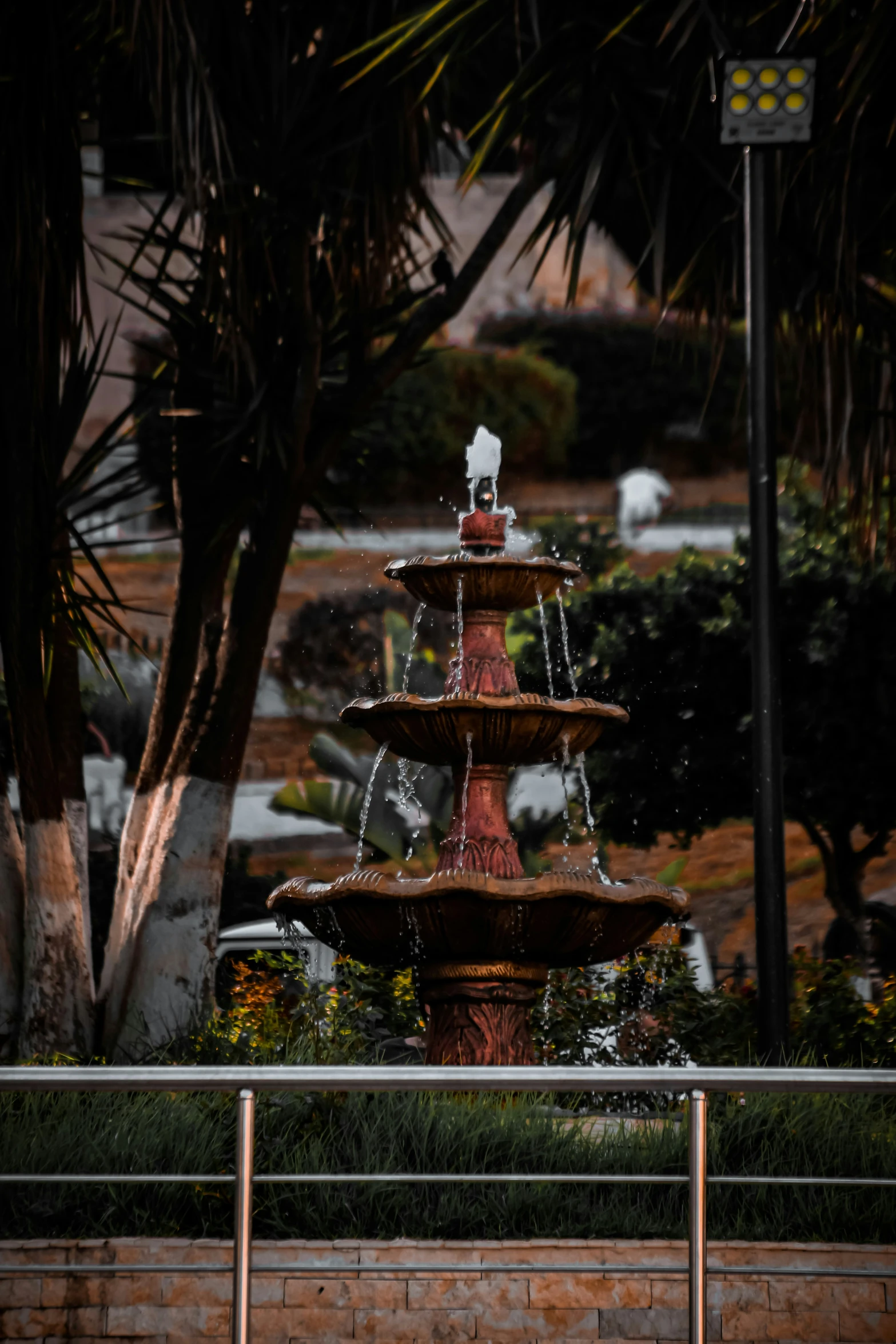 a water fountain with three levels has a fountain and palm trees