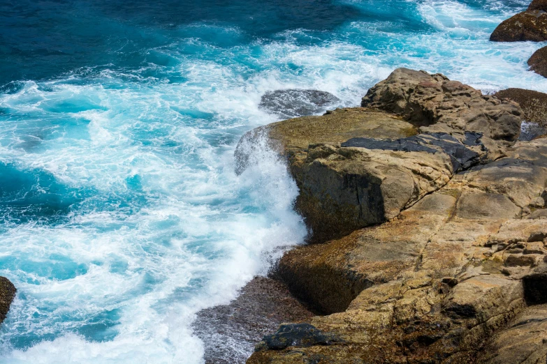 waves crash against large rocks on the edge of a beach