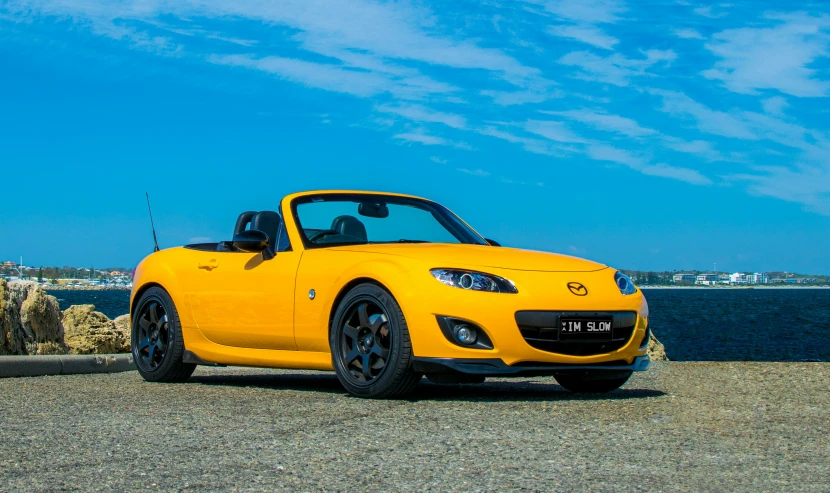 the yellow mazda mia roadster is parked on the side of a beach road