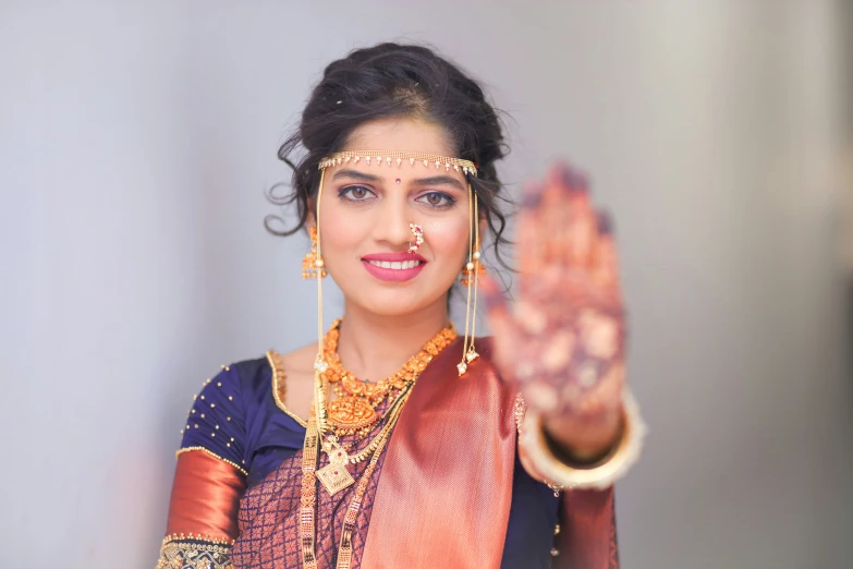 woman dressed in a red silk sari and jewelry with white jewels on her forehead smiles and waves