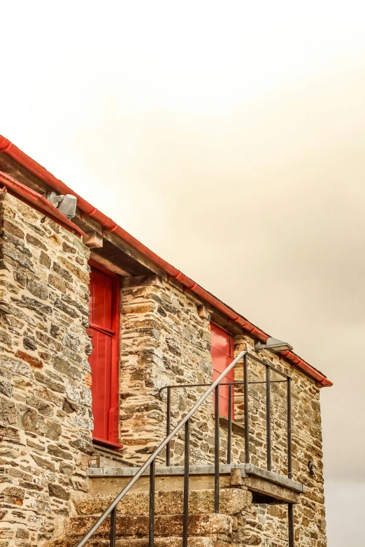 an old stone building with a red door and metal railing