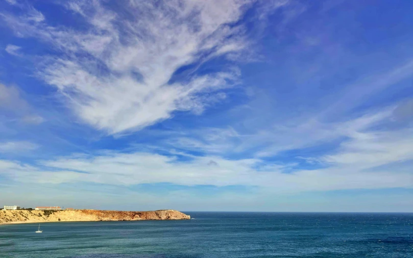 clouds are over the ocean and hills under a blue sky