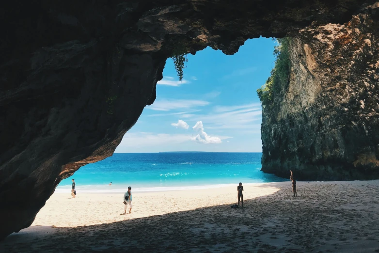 three people walking down the beach in front of a rock cave