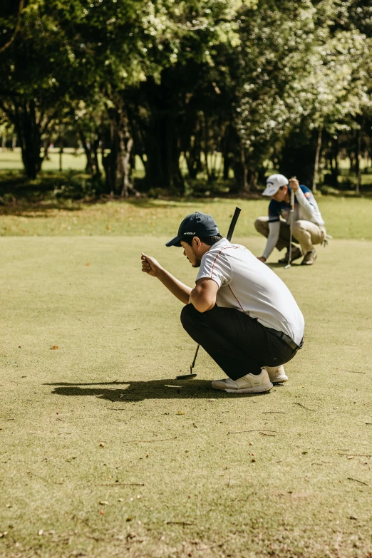 man crouches in the grass as two other players look on