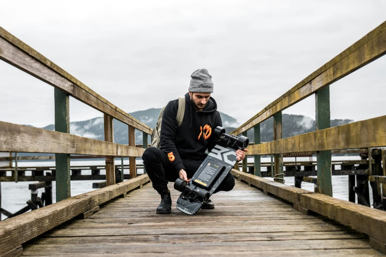 a man holding a skate board on top of a wooden bridge