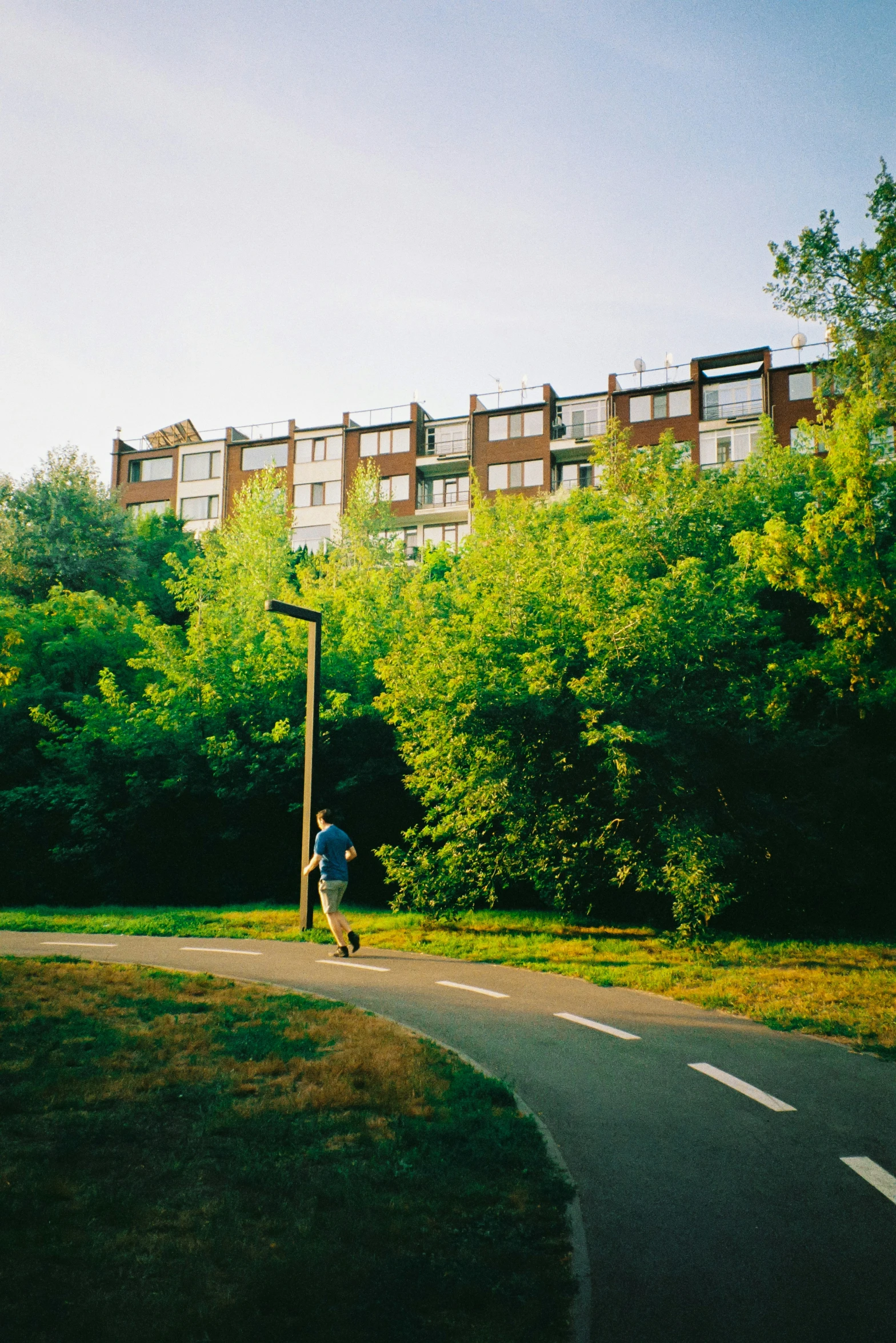 a skateboarder rides past a road beside apartments