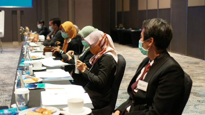 people in business suits are sitting down at tables with masks