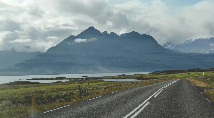 a wide empty road next to a mountain in the middle of nowhere