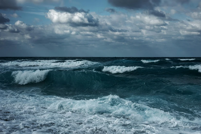 a big wave breaking in on the ocean with the sky above