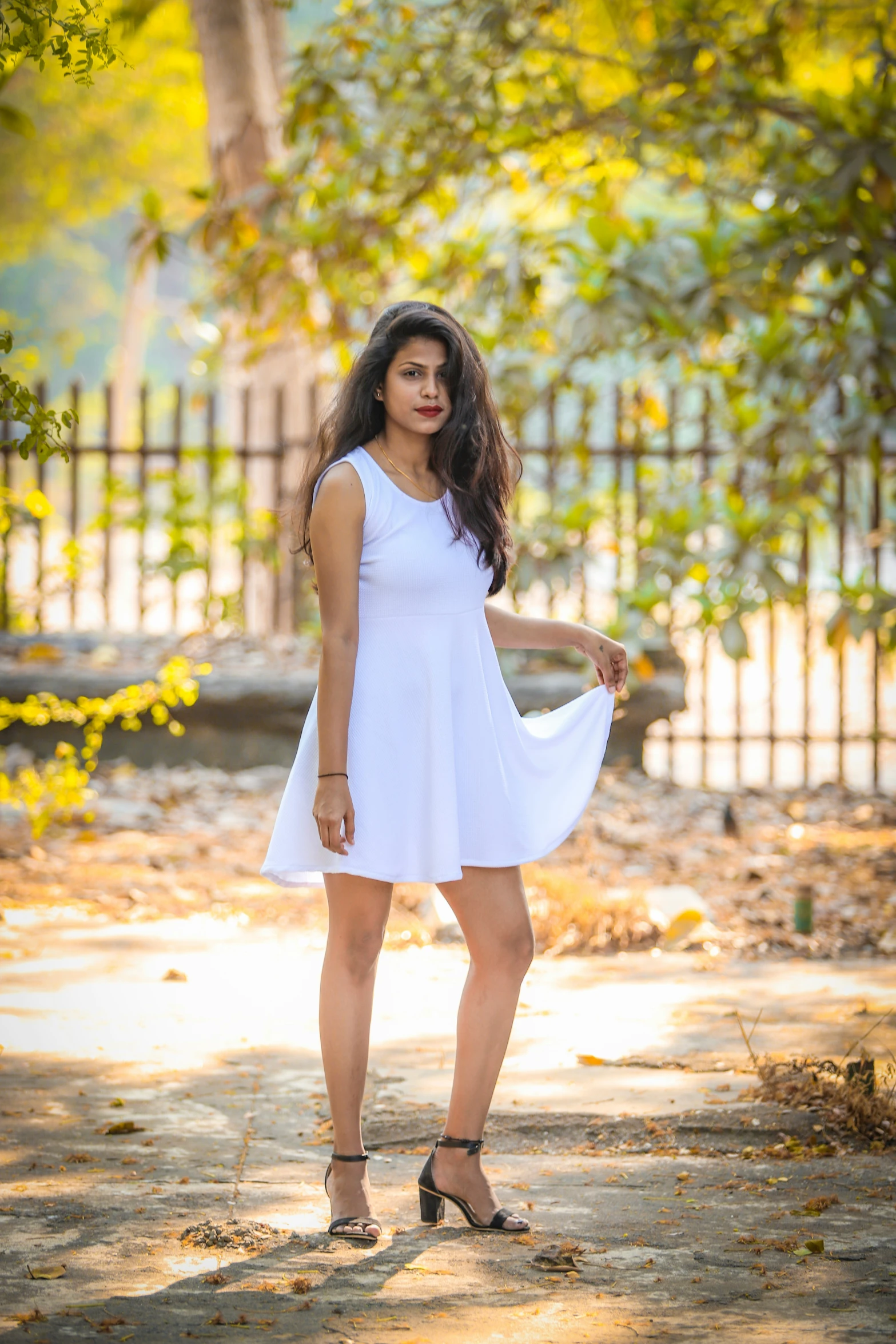 a young woman stands in a park wearing a white dress