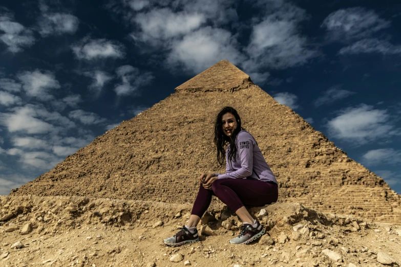 a woman sitting on top of a rocky hill near a pyramid