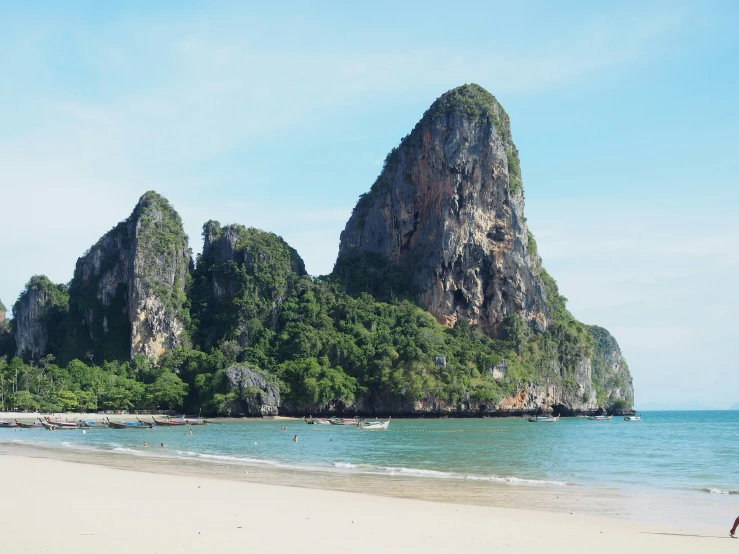 a beach area with several small rocks, a person, and several people walking around