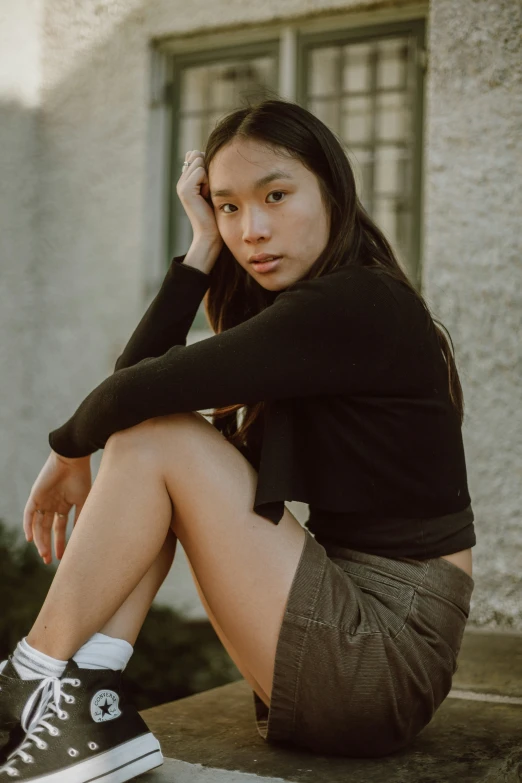 young asian woman wearing dark clothes sitting on a ledge