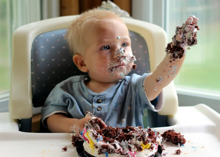 a baby in high chair eating a piece of cake