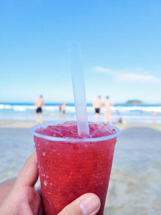 someone holding up an frozen beverage with ice on the beach