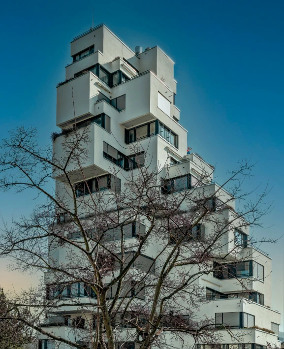 a tall white building next to a tree and some building with balconies