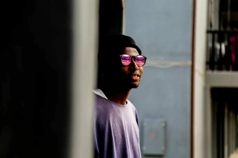 the young man with the pink glasses stands behind the door