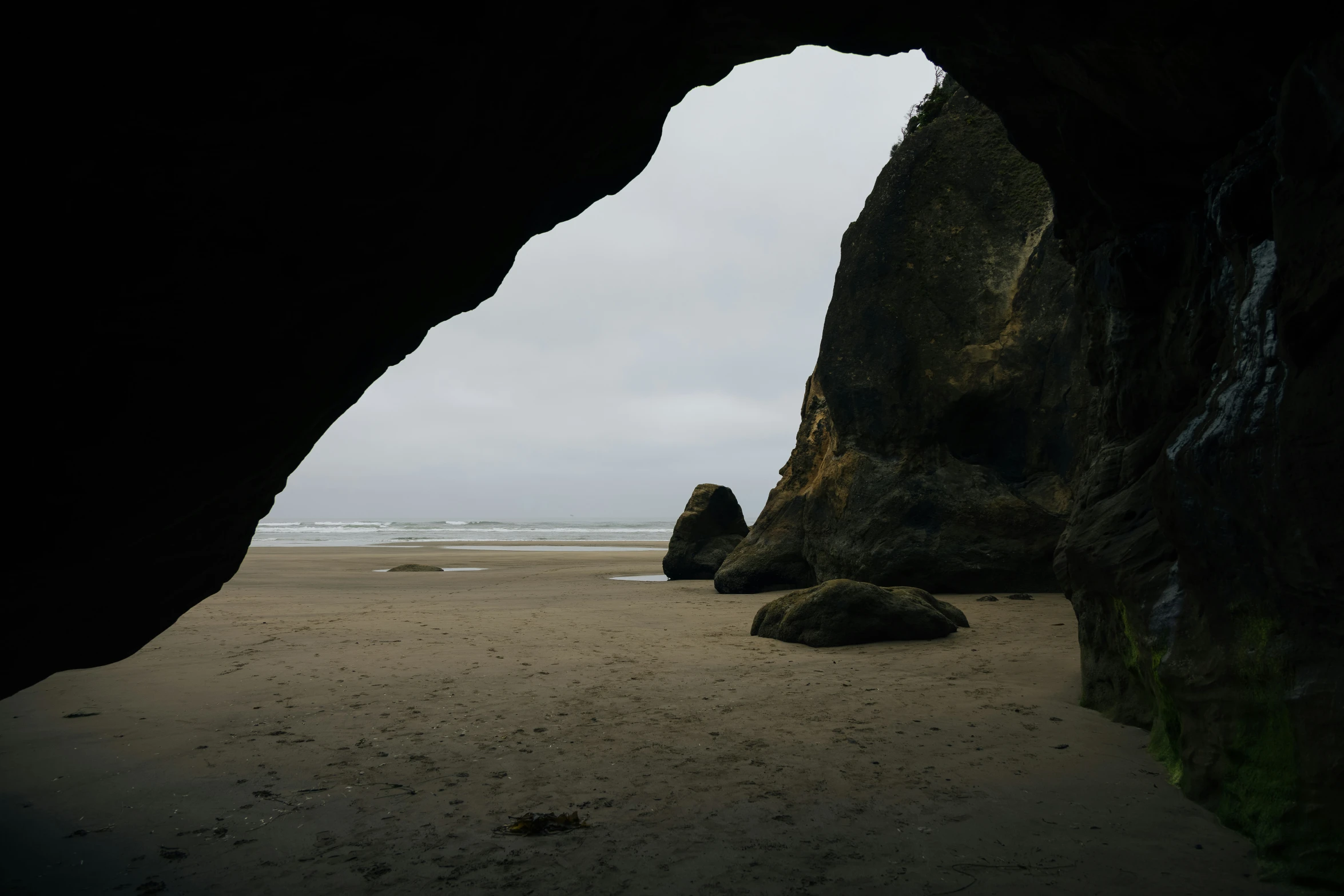 a man walks on a beach past a rock formation