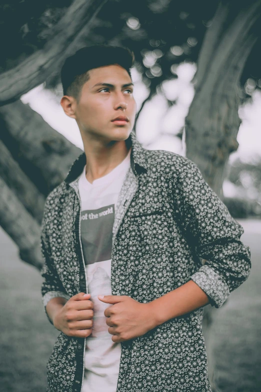 a boy in a jacket stands in front of a tree